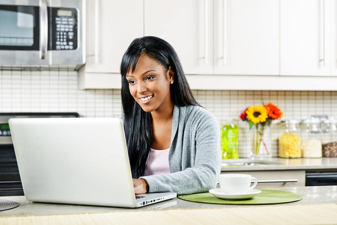 Smiling black woman using computer in modern kitchen interior