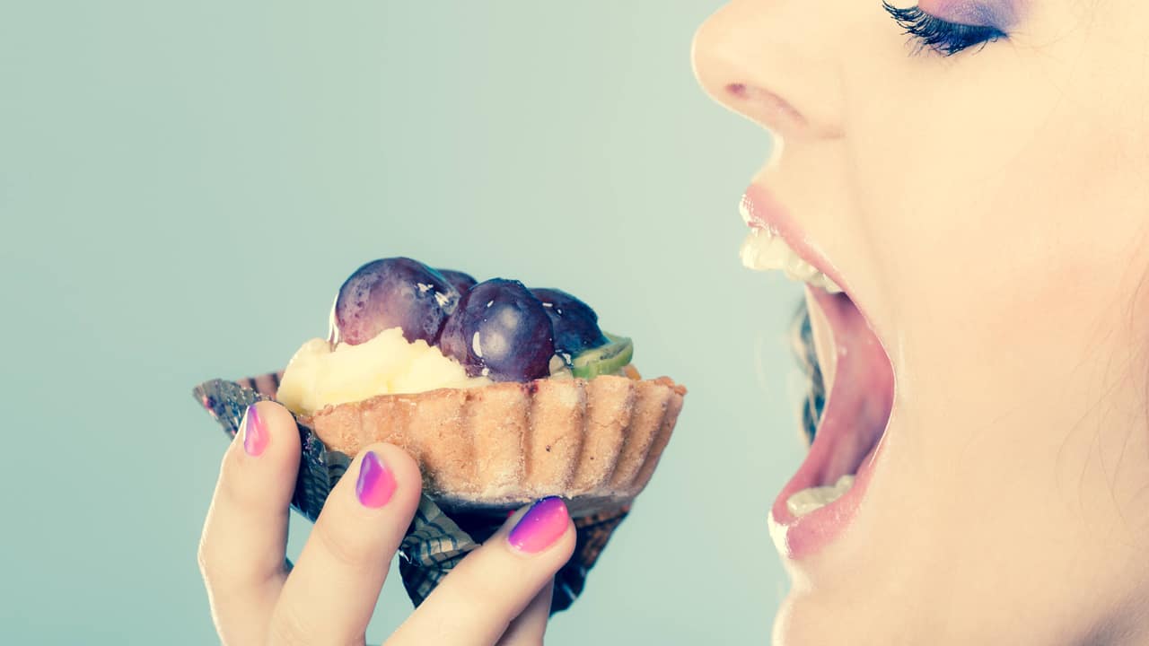 Sweet food indulging and fattening concept. Woman face profile wide open mouth eating cake cupcake filtered photo