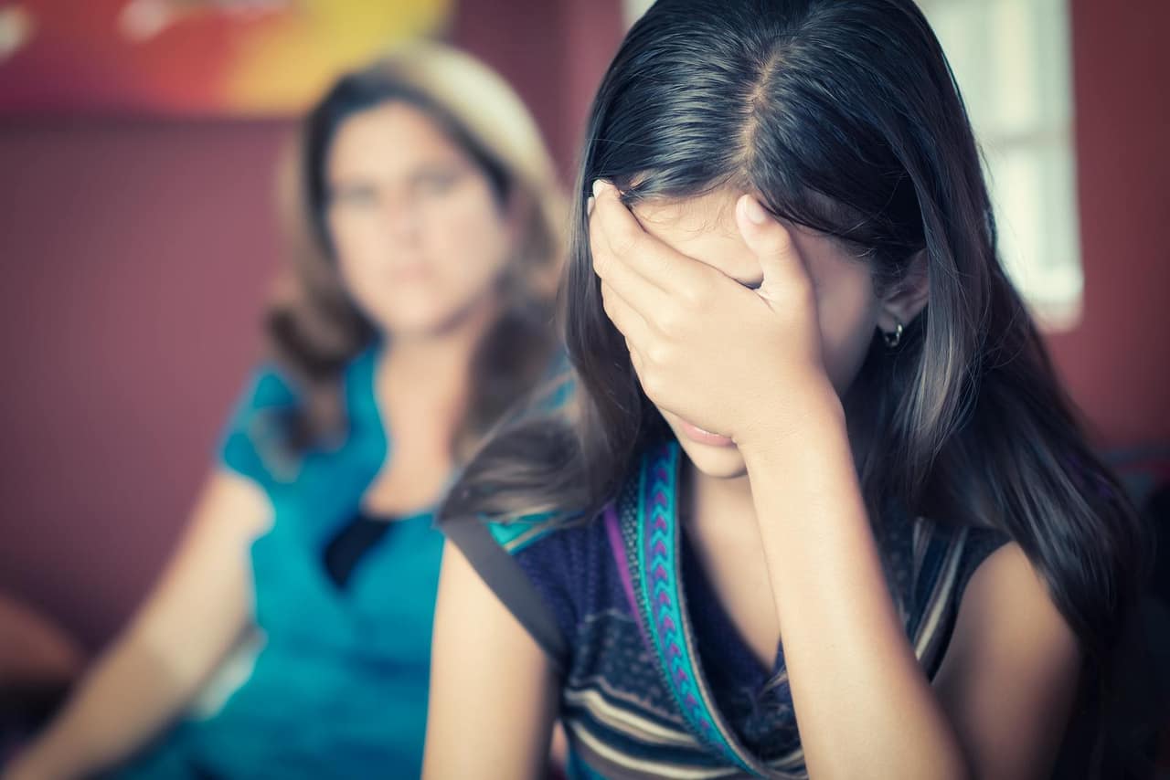 Teenager problems - Teenage girl cries while her mother looks at her on the background