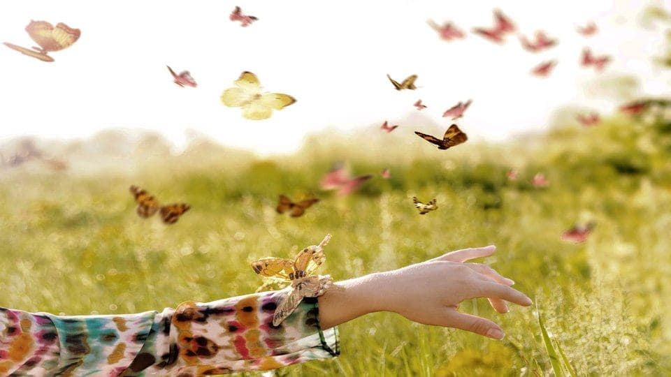 Girl sitting in a meadow in swarm of flitting butterflies.