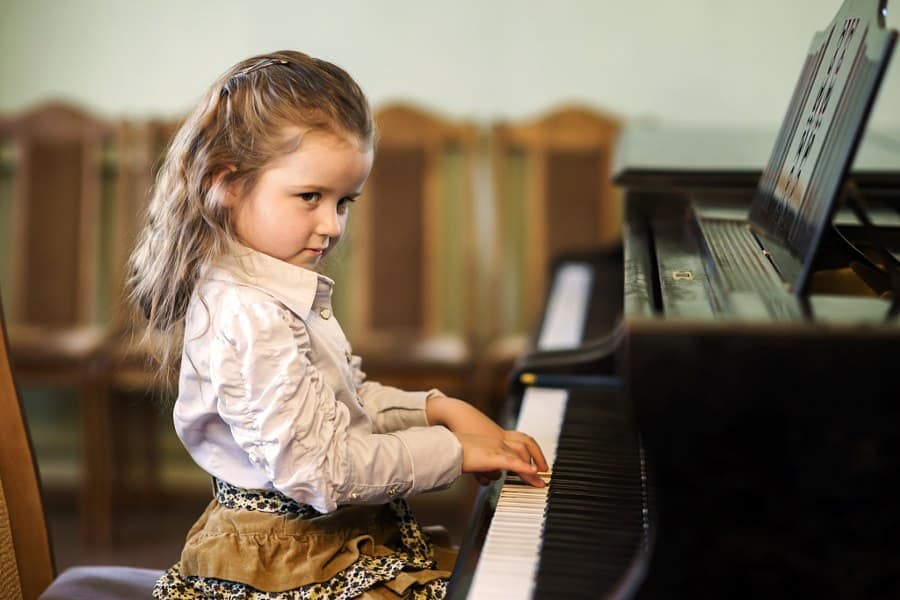 Cute little girl playing grand piano in music school, childhood concept