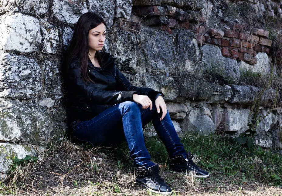 Lonely teenager looking off into the distance, sad expression face, leaning on stone wall.