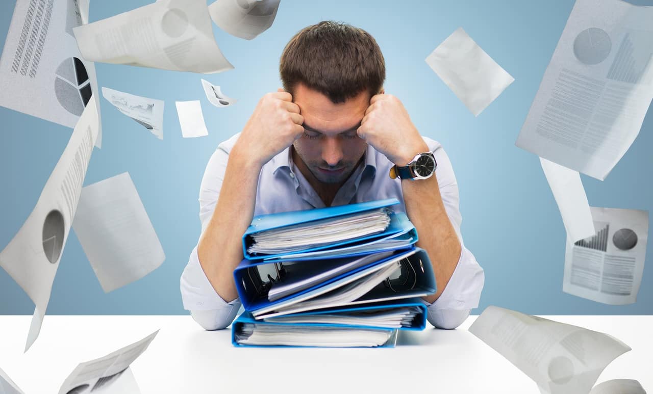 business, people, deadline, stress and paperwork concept - sad businessman with stack of folders and falling papers over blue background
