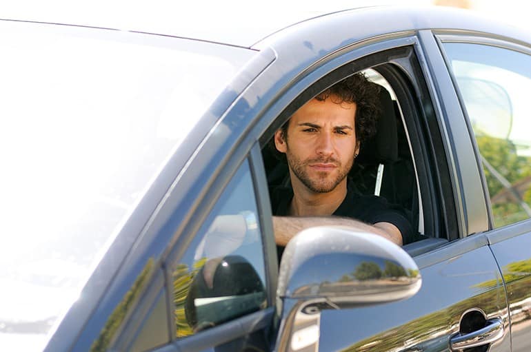 Portrait of a young man driving a car, looking in the rearview mirror