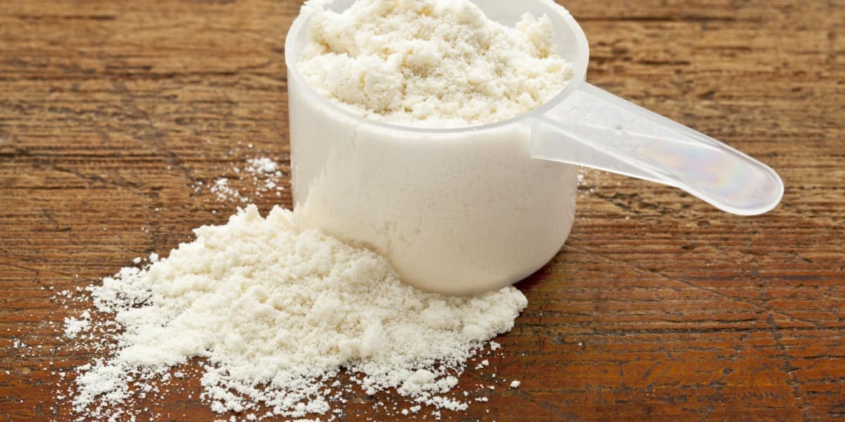 plastic measuring scoop of white powder (whey protein) against grunge wood background