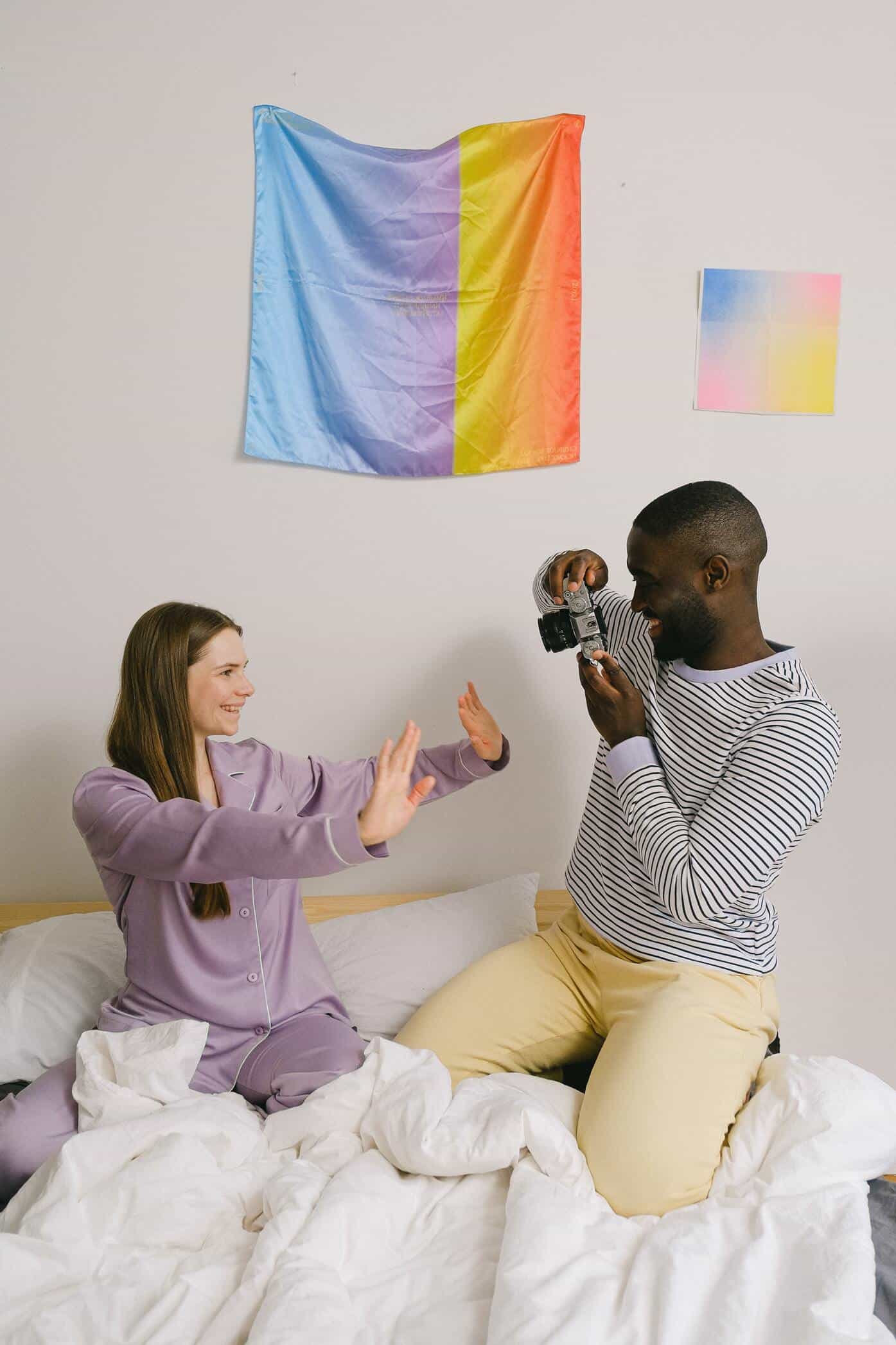 cheerful black man taking photo of girlfriend in bedroom