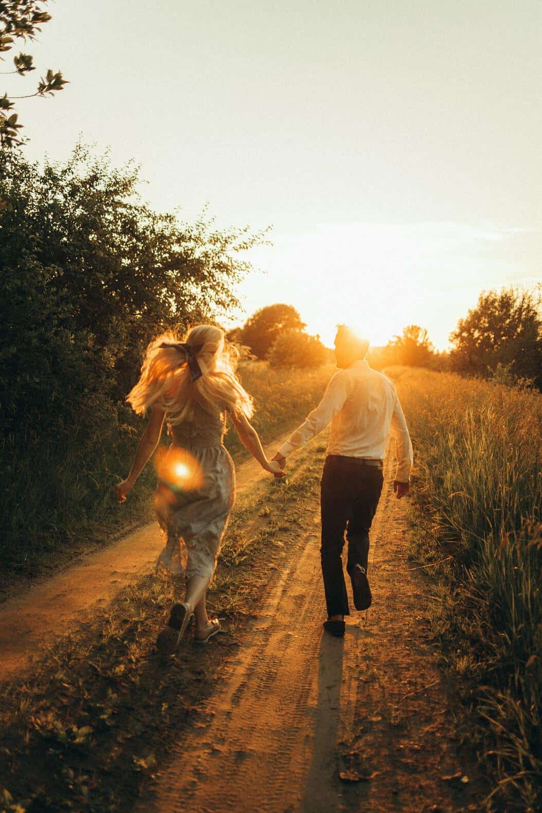 couple holding hands while running towards the sunset