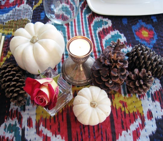 white pumpkins, pine cones, tealight candle, and a flower on top of an ikat cloth