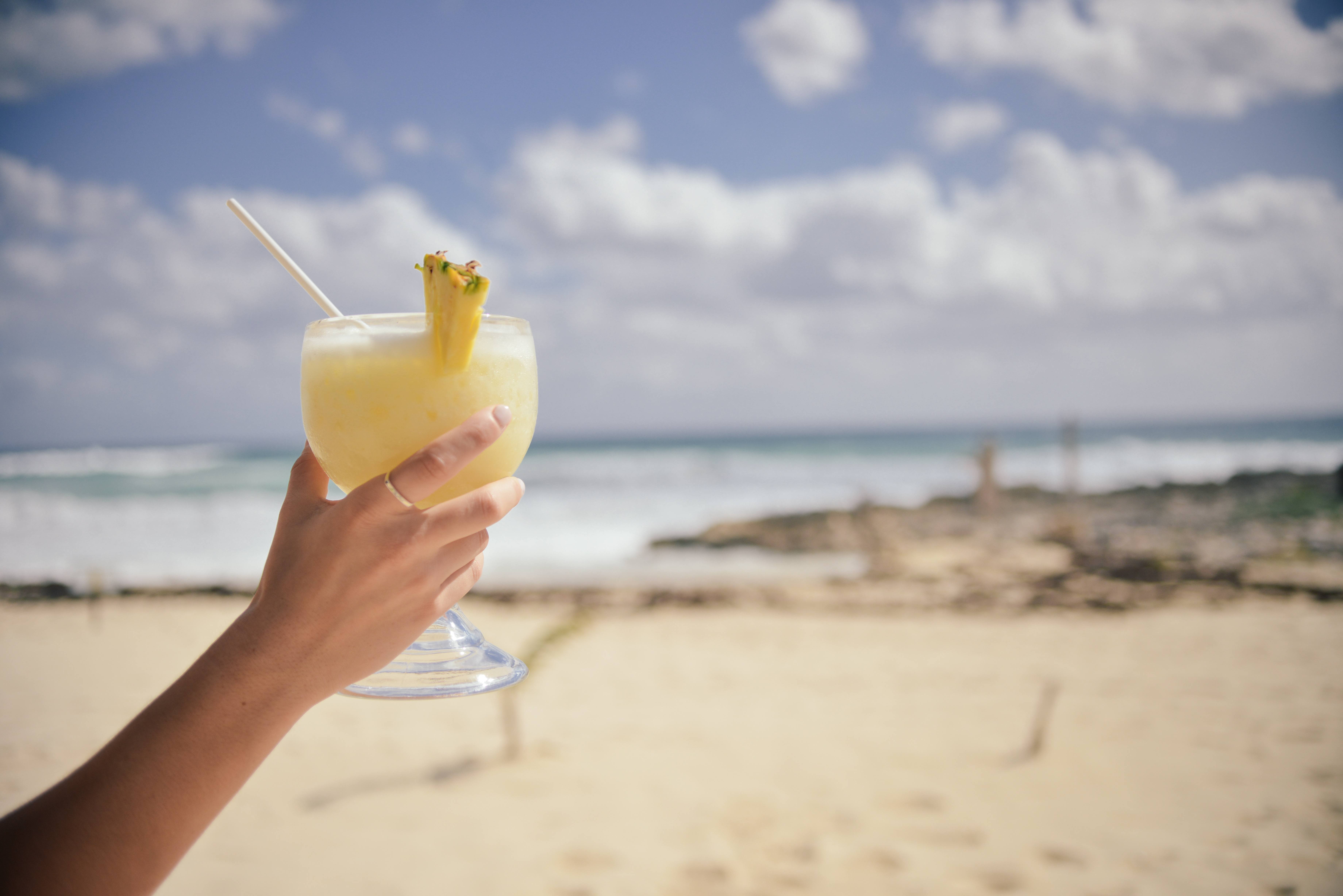 Womans Hand Holding Cocktail On Beach