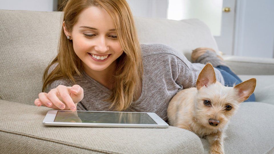 Image of a girl relaxing with her iPad beside a puppy