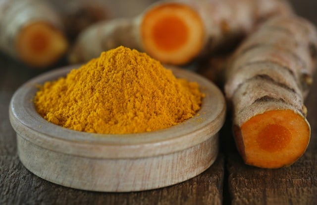 Raw and ground turmeric on wooden surface