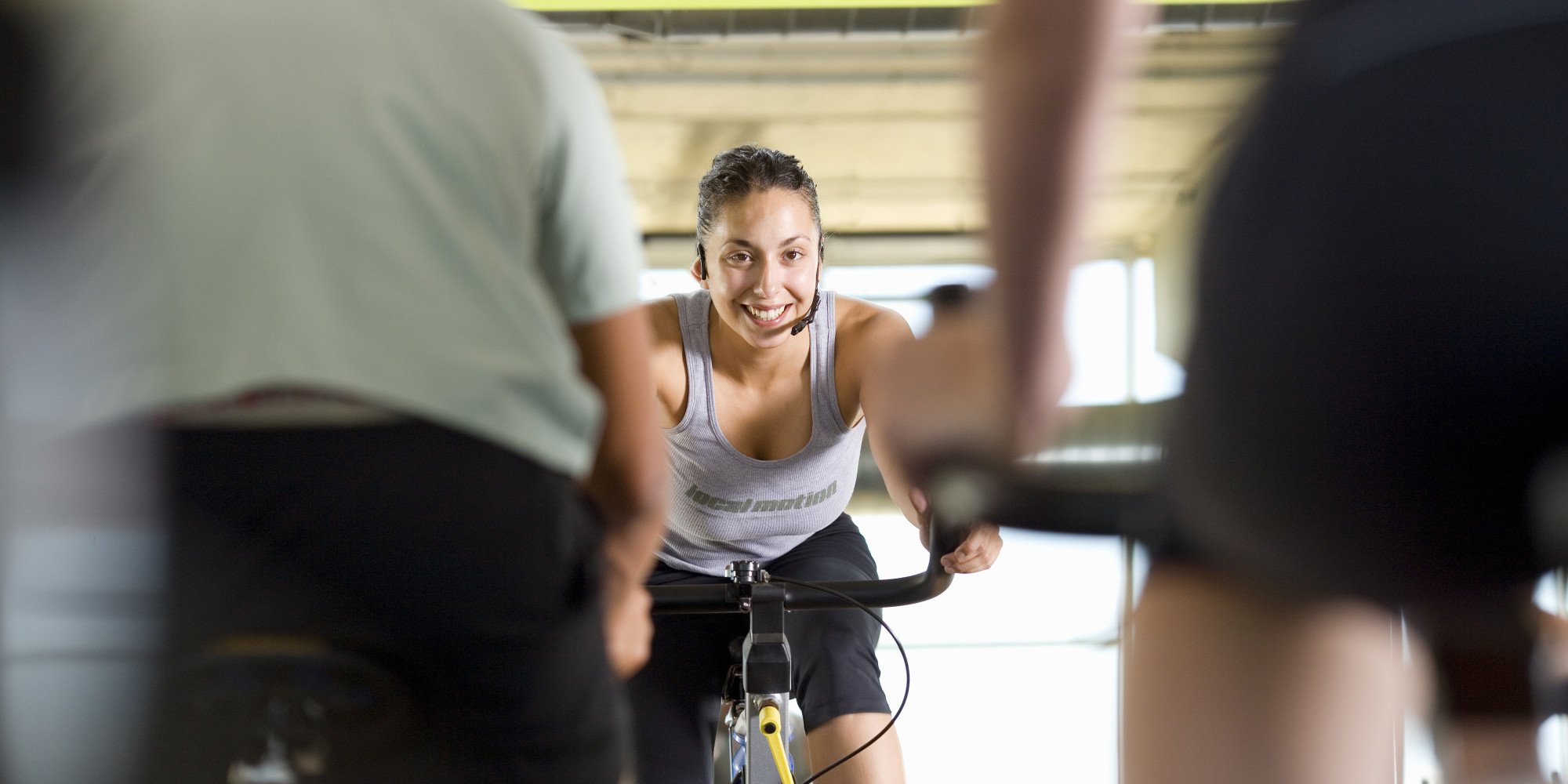 Fitness instructor leading class on exercise bicycles in gym, low angle view