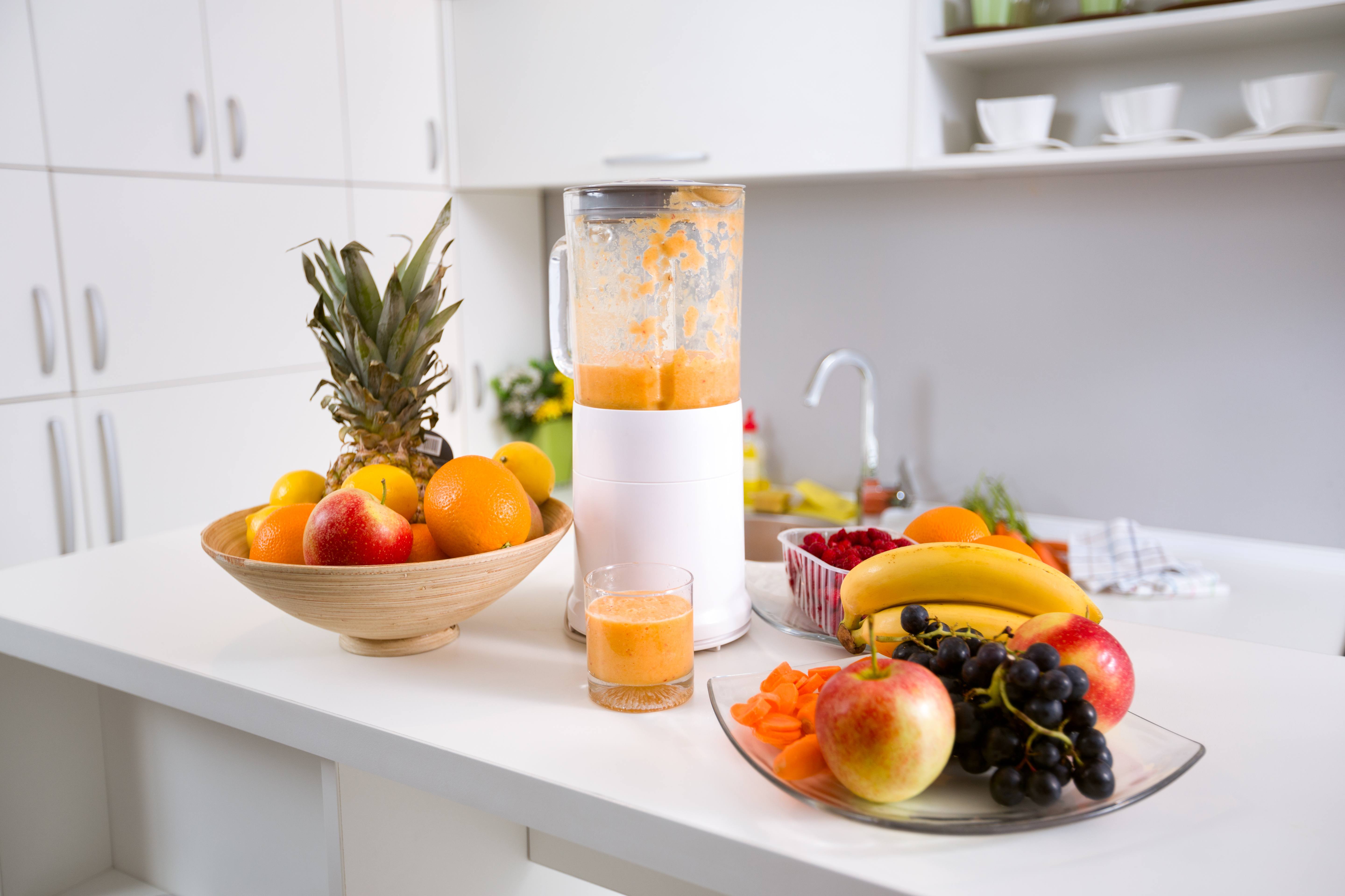 healthy smoothie ingredients in blender with fresh fruit on kitchen table