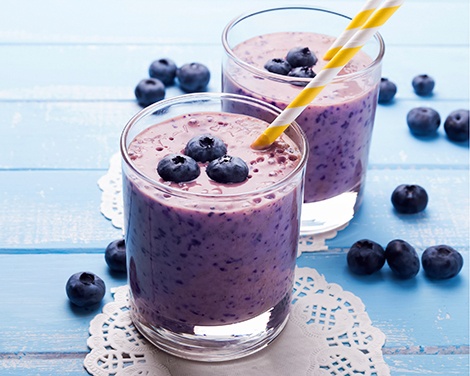 Two glasses of blueberry smoothie on blue colored wooden table
