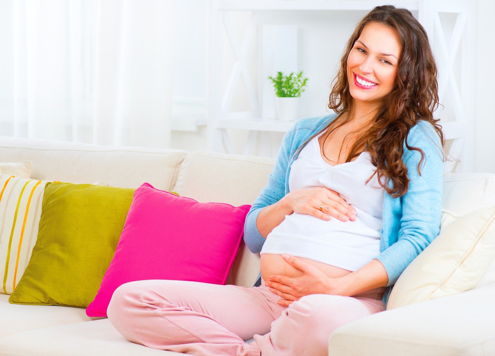 Pregnant Happy smiling Woman sitting on a sofa and caressing her belly. Mom Expecting Baby. Pregnant Woman Belly. Pregnancy. Beautiful Pregnant Woman. Maternity concept. Baby Shower