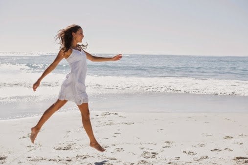 Happy brunette in white sun dress skipping on the sand