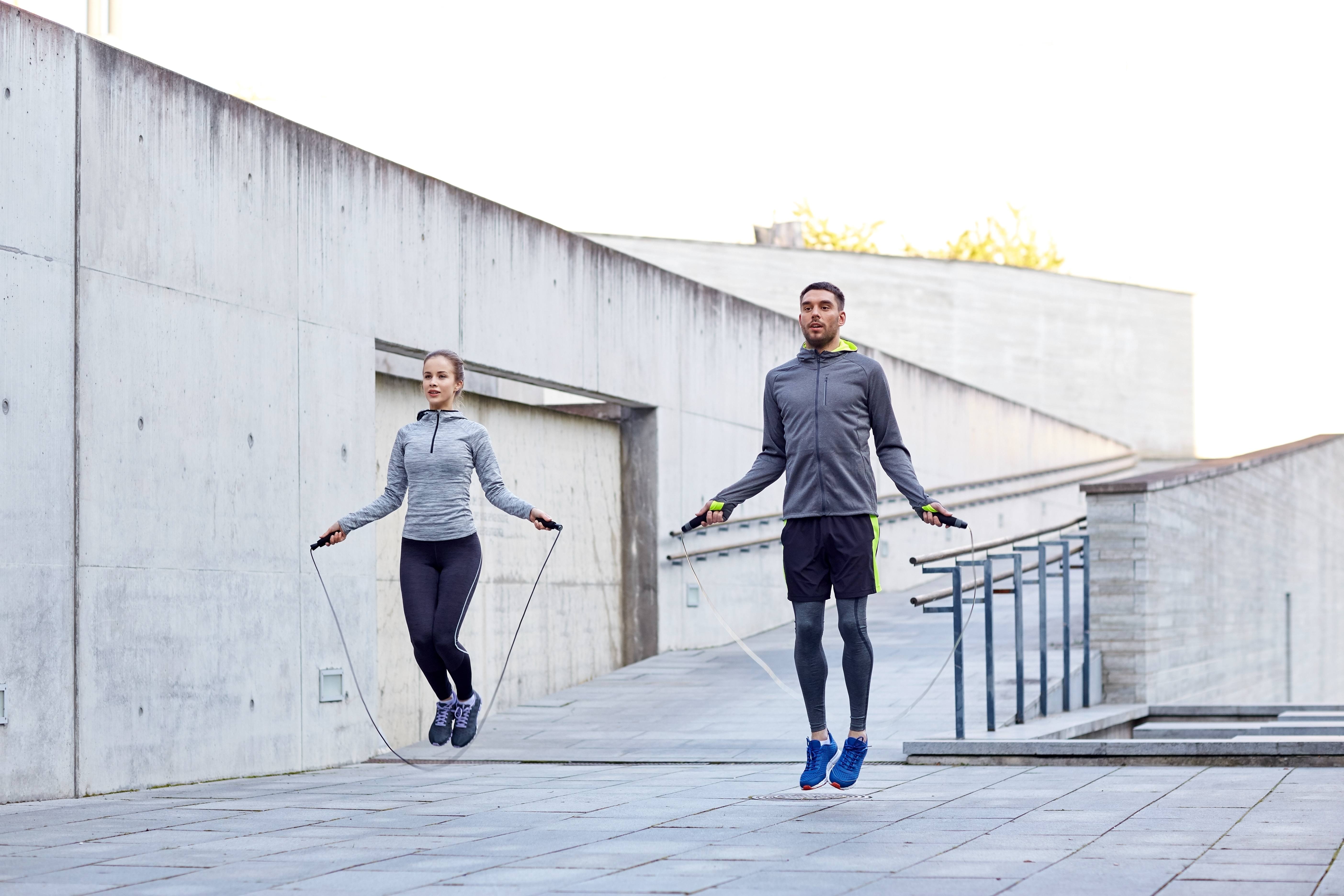 fitness, sport, people, exercising and lifestyle concept - man and woman skipping with jump rope outdoors