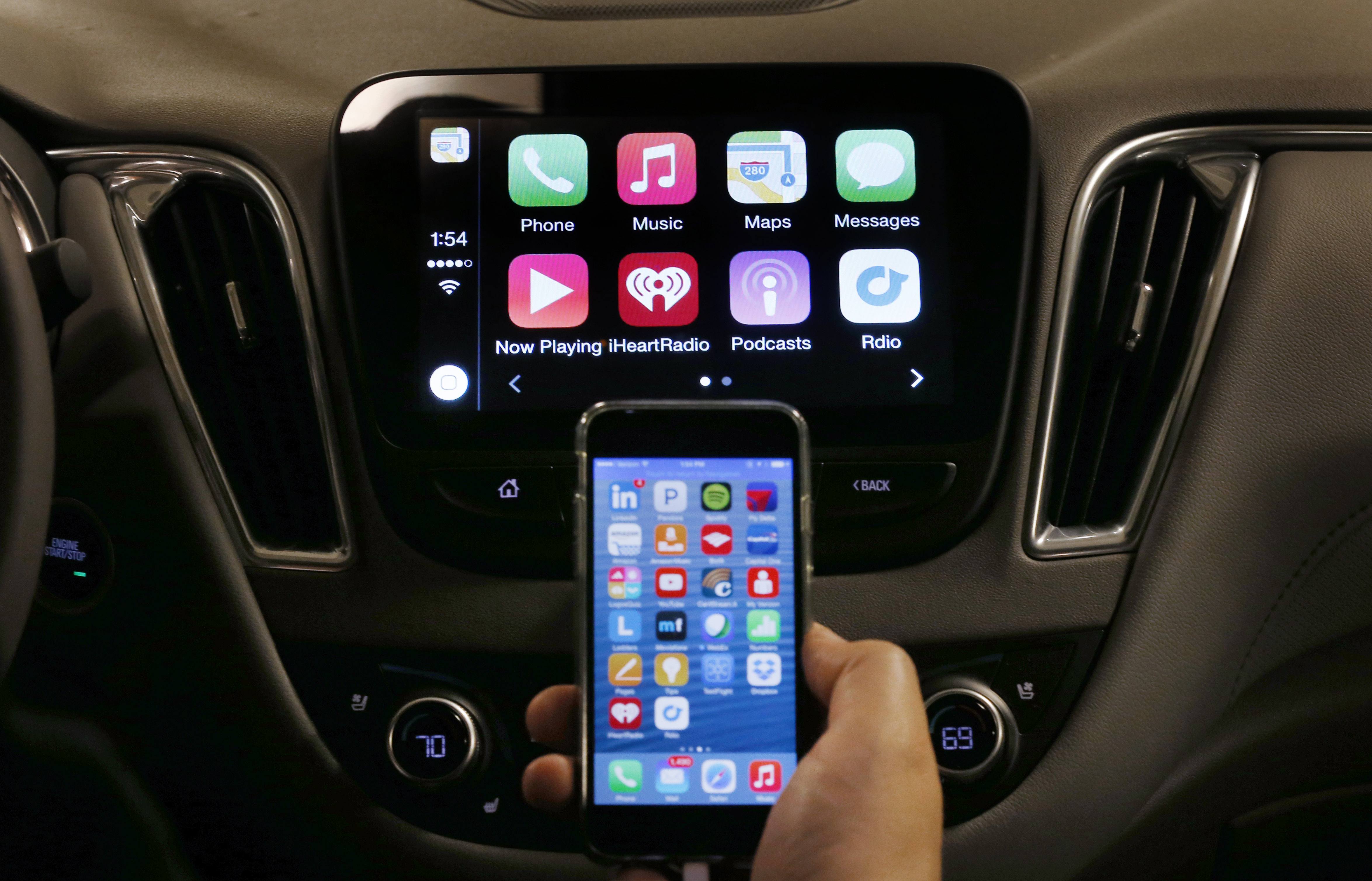 An iPhone is connected to a 2016 Chevrolet Malibu equipped with Apple CarPlay apps, displayed on the car's MyLink screen, top, during a demonstration in Detroit, Tuesday, May 26, 2015. Starting with Chevrolet this summer, many General Motors models will offer AppleÂ’s CarPlay and GoogleÂ’s Android Auto systems that link smart phones with in-car screens and electronics. (AP Photo/Paul Sancya)