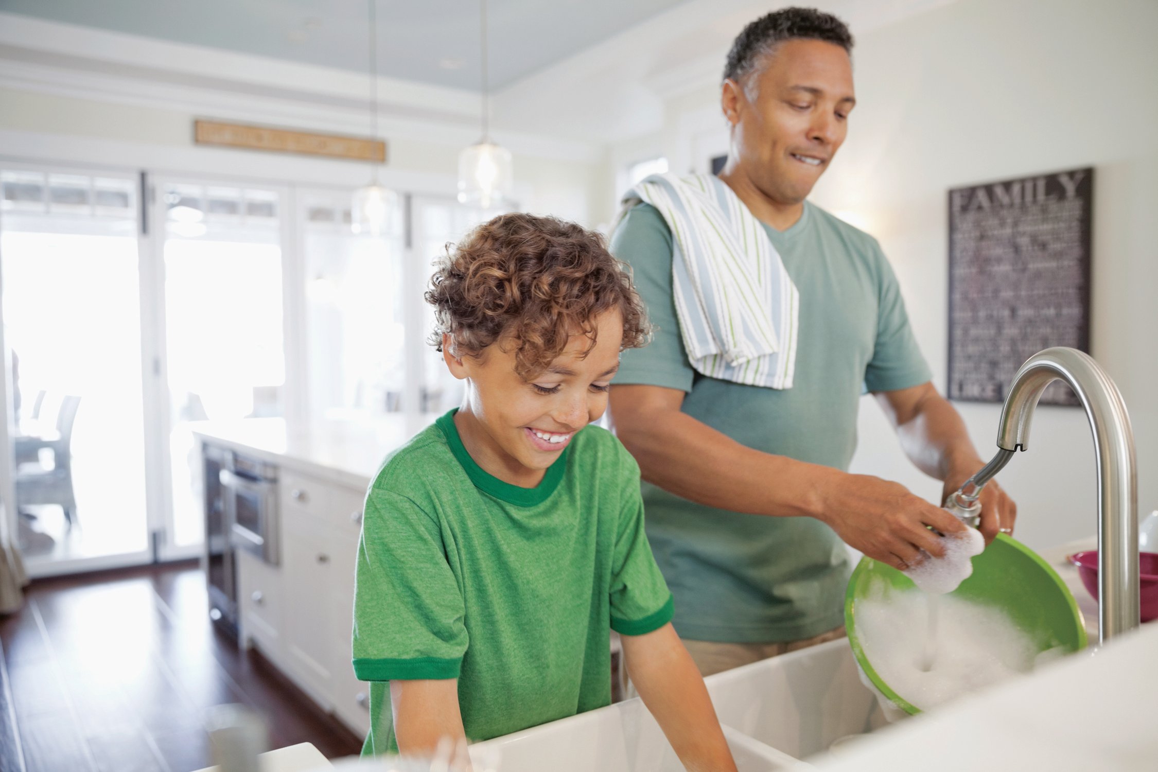 Mature father and son washing dishes together at kitchen sink