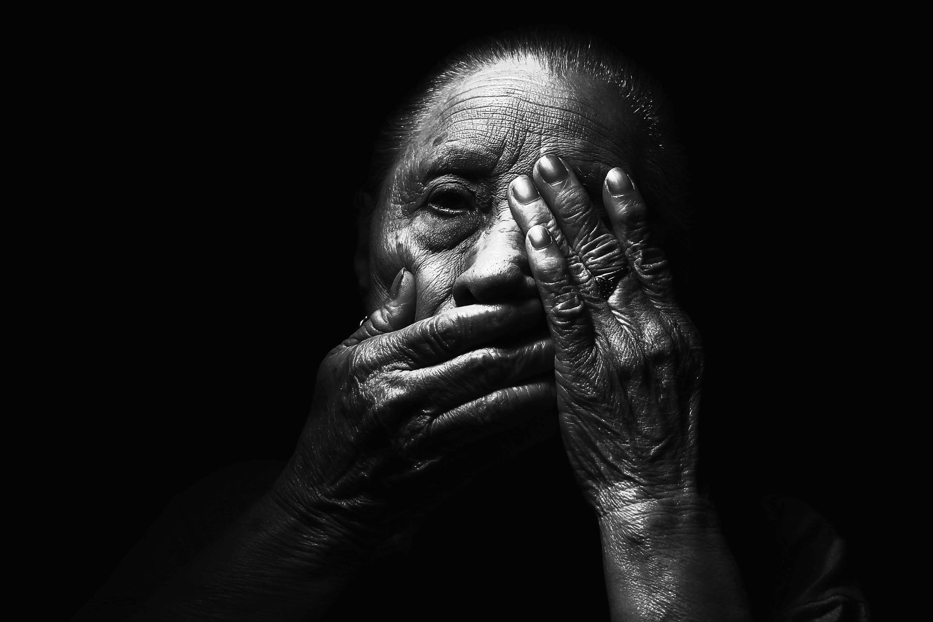 Woman places a hand over her mouth and eyes in low light, greyscale image