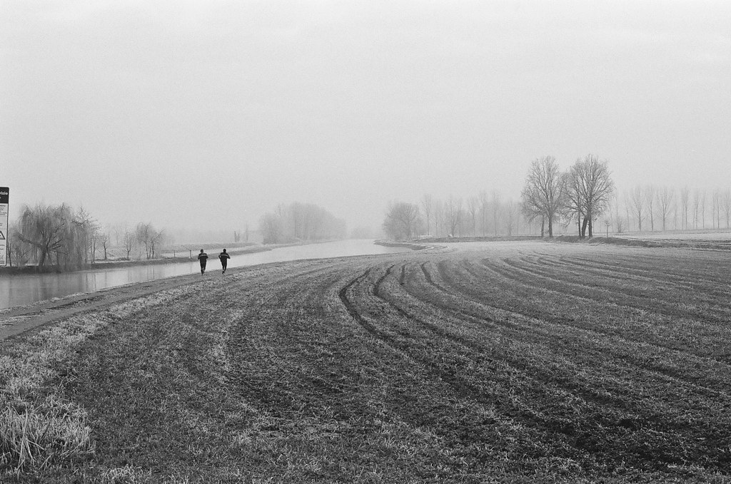 Two runners in the distance jog around a field that has recently been ploughed
