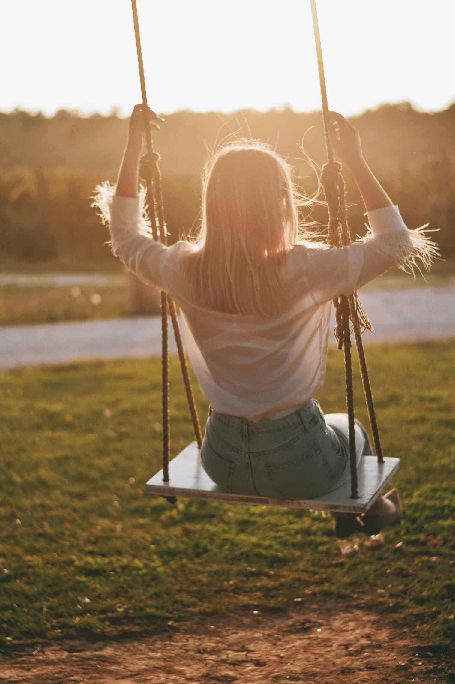 woman in white long sleeves sitting on swing during daylight